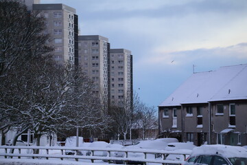 Urban winter scene with residential skyscraper buildings in the background and lamp posts.Urban winter scene with residential skyscraper buildings in the background.Bare trees,snow on the ground