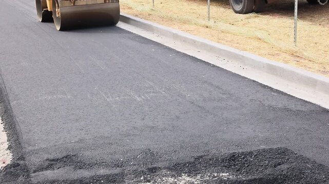 Large roller compacted freshly laid asphalt on road during road construction asphalt paving