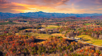 Scattered houses and homesteads in vibrant forest in fall season on Appalachian mountain range.