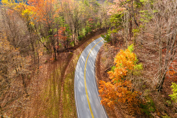 Naklejka premium Scenic drive through Tennessee Appalachians at sunset in fall season. Car traveling on curvy forest road under vibrant autumn foliage