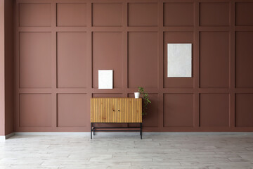 Commode with plant and paintings on brown wall in room