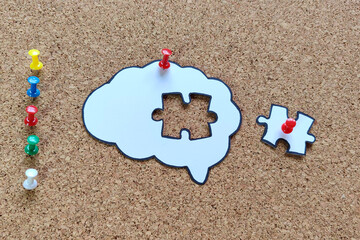 Missing puzzle piece completing a brain symbol on a cork board. Mental health and problems with memory.