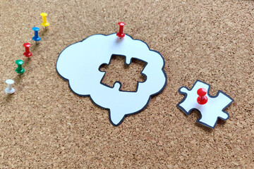 Missing puzzle piece completing a brain symbol on a cork board. Mental health and problems with memory.