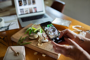 Adult artisan photographing handmade jewelry at home, focused