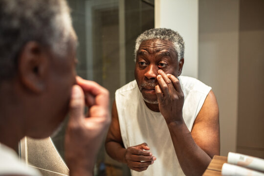 Senior man checking eye with focused expression in home bathroom