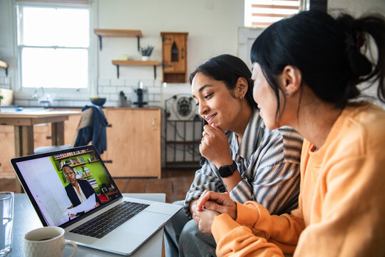 Young lesbian couple focused on video call at home kitchen