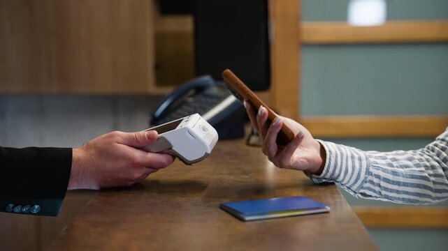 Guest using contactless smartphone payment at hotel reception desk