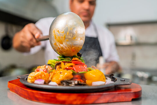 Chef pouring sauce over sizzling chifa wok dish