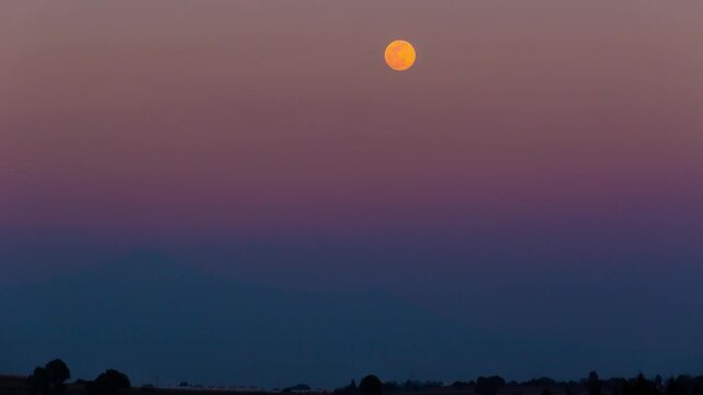 Full orange moon setting behind malinche volcano
