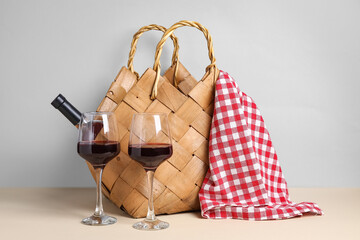 Rattan picnic basket with bottle of wine and glasses on beige table against grey wall