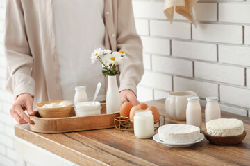 Young woman with tray and different dairy products in kitchen