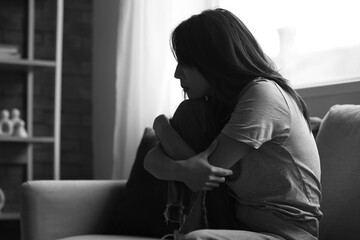Sad young Asian woman sitting on sofa at home. International Stress Awareness Week