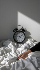 Vintage alarm clock on white bedding with a woman's hand resting nearby, symbolizing time and mental health