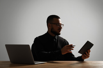 Silhouette of young businessman with laptop and tablet computer at table on grey background. Data science concept