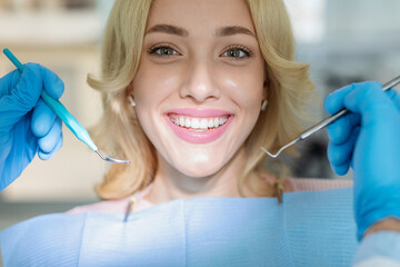 Closeup of beautiful young lady showing her white teeth while having checkup at dental clinic,...