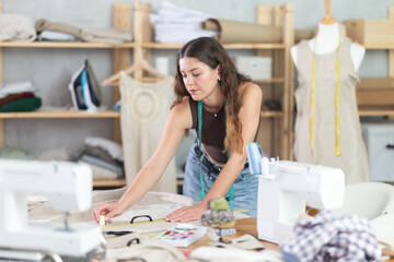 Woman tailor makes chalk markings on the fabric before cutting. Process of sewing clothes in a...