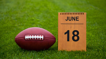 Obraz premium American football on a grass field next to a wooden calendar displaying the date june 18
