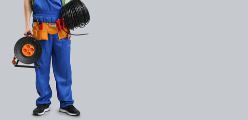 Male electrician with extension cable reel and wires on grey background