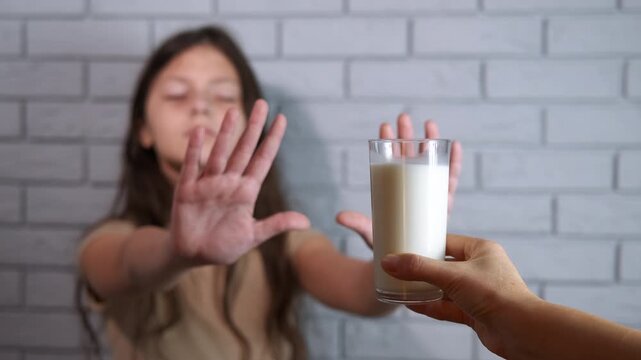 Lactose intolerance. Unhappy young girl with lactose intolerance refusing a glass of milk offered to her, expressing aversion and discomfort with a stop gesture and a disgusted look on her face