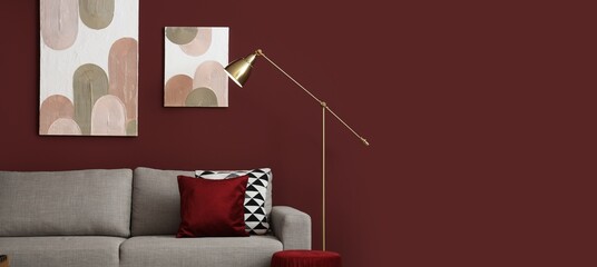 Obraz premium Interior of stylish living room with cozy sofa and lamp near red wall. Banner for design