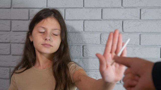 Young girl refusing cigarette offered by adult. Determined young girl making a conscious decision for a healthy lifestyle, gesturing to stop and refusing a cigarette offered by an adult hand