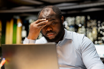 Black male employee dealing with fatigue and burnout after hours in the office, struggling to stay...