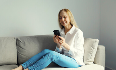 Obraz premium Happy mature woman looks at phone, girl with smartphone sitting on the couch in room at home