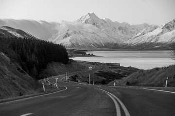 Windy road next to a lake leading to a big snow covered mountain