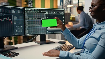 Prop firm intern in office learns new trading strategies from video lesson on green screen mobile phone. Brokerage company trainee using chroma key smartphone to watch educational content