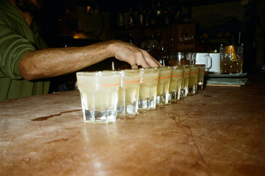 Hand reaching for a row of yellow liquor shots at a bar
