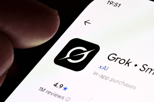 Grok AI app listing on smartphone screen with xAI logo and rating, extreme macro close-up with finger touching display. Stafford, United Kingdom, January 7, 2026,