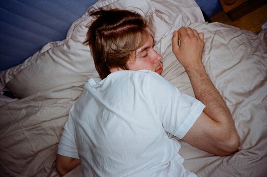 Young man sleeping peacefully in bed with rumpled white sheets

