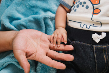 Hand of a baby holding the fingers of an adult hand.