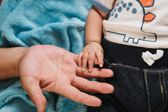 Hand of a baby holding the fingers of an adult hand.