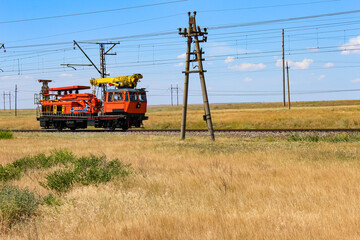 Orange railway maintenance vehicle working on tracks in a rural landscape. Railway infrastructure, maintenance and repair works, and rail transportation concept.
