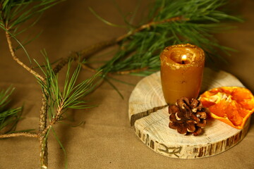 Burning Christmas wax candle on wooden candlestick near natural cone, dried orange on table with green natural fir branch. Home cozy aromatherapy relax eco ornament. Closeup