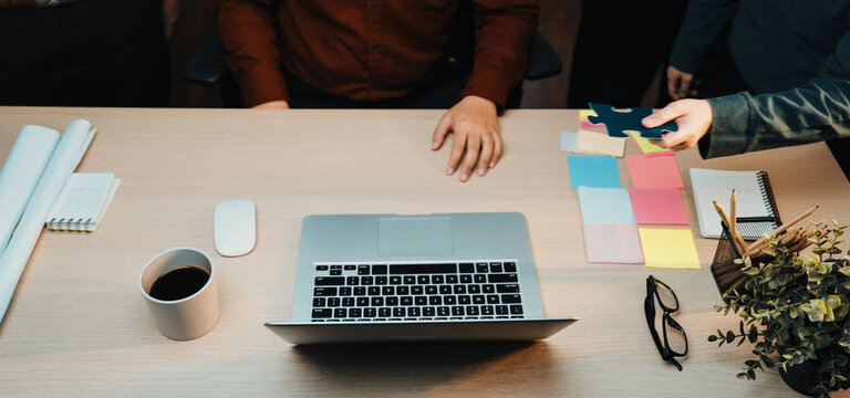 A vibrant scene of diverse professionals engaged in teamwork around a modern office desk, showcasing collaboration through colorful puzzle pieces and a laptop, inspiring creativity. SACTR - Powered by Adobe