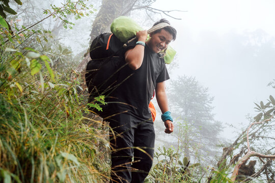 Portrait of strong Sherpa man working as porter carrying huge cargo with traditional method on forehead. High Himalayas expedition during Mera peak climbing. Transportation or goods delivery concept