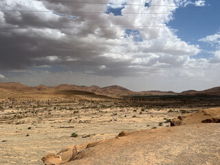 Panoramic view of a rocky desert plateau and distant mountains under a cloudy sky in the Algerian Sahara.