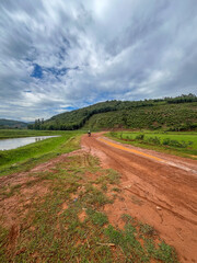 Winding red dirt road passing by a calm lake and green hills with a motorcycle in the distance in rural Rwanda.