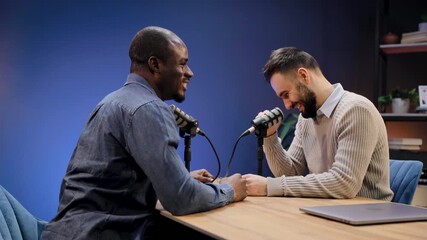 Two multiracial men engaging in a lively discussion and interview, recording a podcast with microphones in a modern studio
