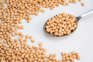 Metal spoon filled with dried chickpeas on white background, scattered legumes creating a frame,...