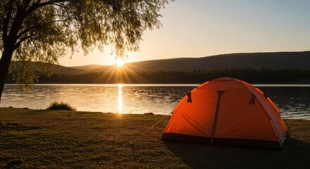 A lone orange tent on grassy shoreline by a lake at sunset with tree and mountains