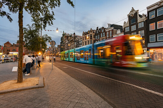 Tram Travels Through Lively Street in Amsterdam During Twilight