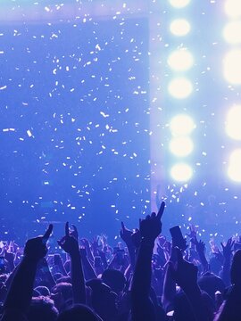 Blue stage lighting and raised hands during a confetti moment