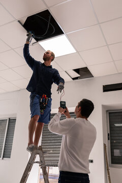 Electricians checking ceiling wiring at office