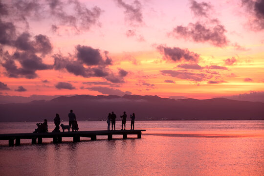 Silhouetted people on a wooden pier at sunset