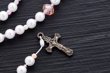 Catholic rosary with white pearls and pink details, accompanied by a metal cross, set against a dark background with soft lighting.