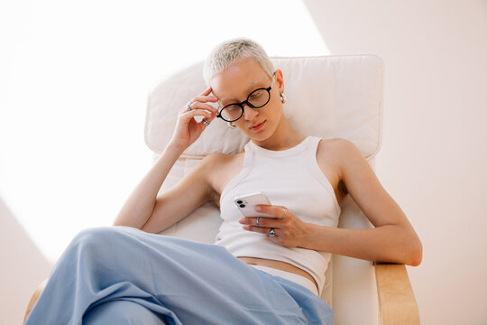 Woman in a tank top and blue pants sitting in a chair with phone