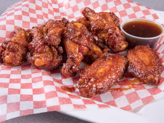 A pound of honey garlic chicken wings and sauce on red checkered paper